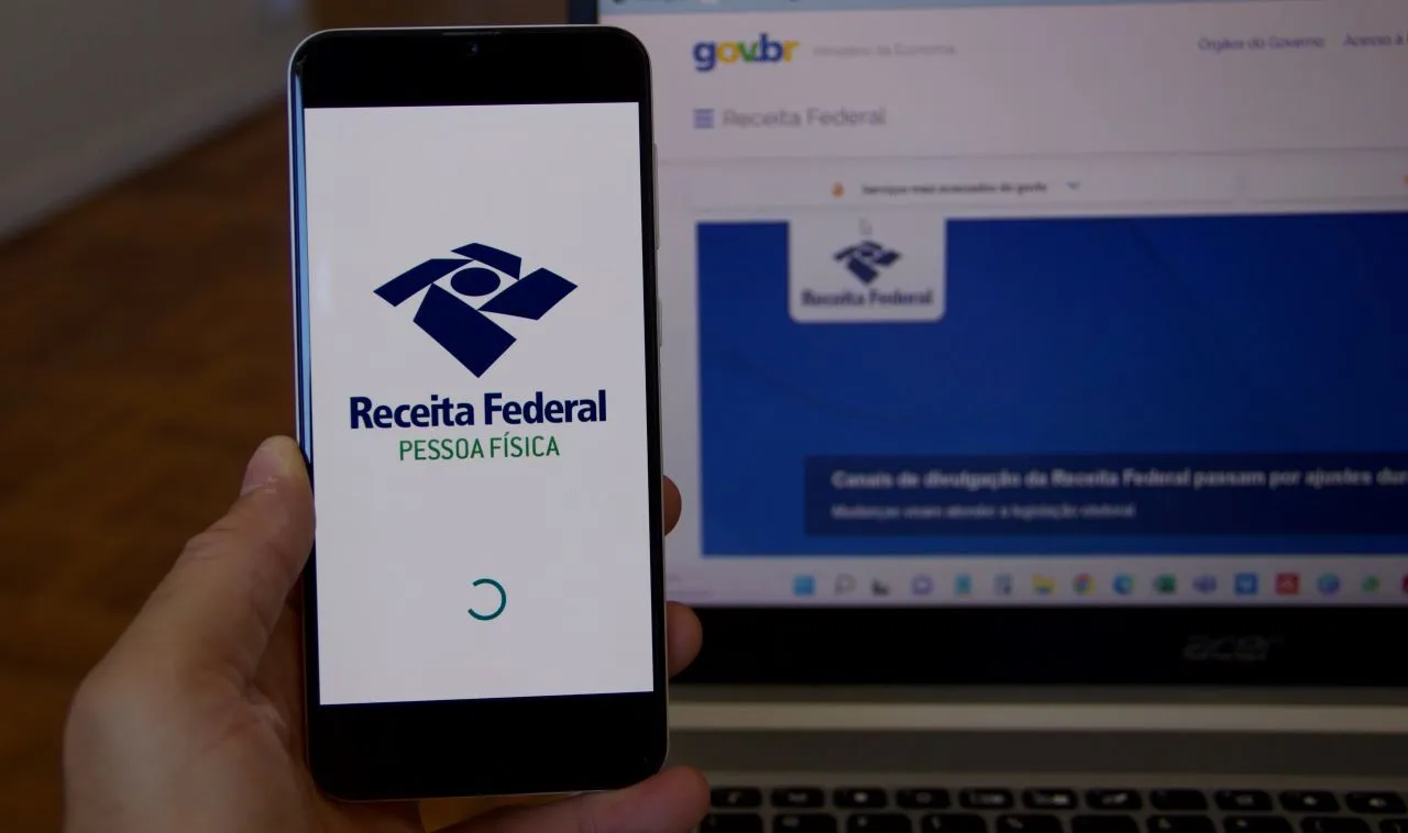 Declaração do imposto de renda | Foto de uma pessoa segurando um celular com o programa da Receita Federal e um computador ao fundo no site da Receita Federal | Certificação Digital | Blog da CertiSign