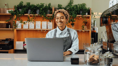 Foto de uma mulher sorrindo utilizando o notebook em uma loja.