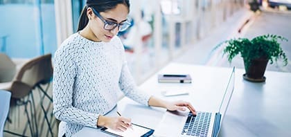 Mulher sentada mexendo em um notebook e em um tabler