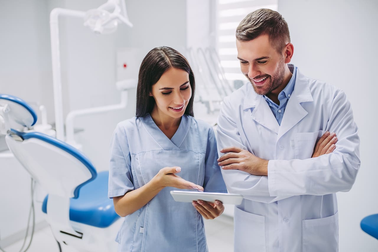 Vantagens da assinatura digital na clínica odontológica | Foto de uma dentista e de um dentista analisando prontuário eletrônico de paciente no tablet | Profissionais da Saúde | Blog da Certisign